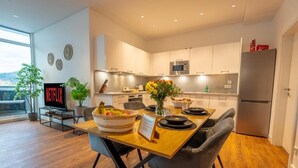 Una cocina moderna con armarios blancos, un refrigerador de acero inoxidable y un comedor con una mesa y sillas de madera.