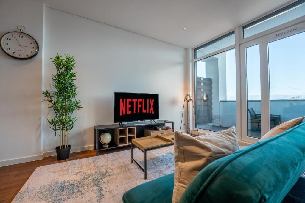 A living room with a large window, a television, a potted plant, and a sofa.