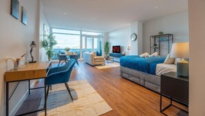 Una habitación de hotel moderna con cama, escritorio, silla y ventanas amplias.