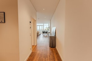 A hallway with a wooden floor, a dining area with a table and chairs, and a view of a cityscape through large windows.