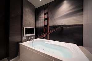 Un baño moderno con una bañera grande, un televisor montado en la pared y un mural del puente Golden Gate.