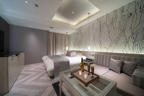 Una habitación de hotel moderna con cama, sofá, una mesa de centro de vidrio y una pared con diseño de hojas.