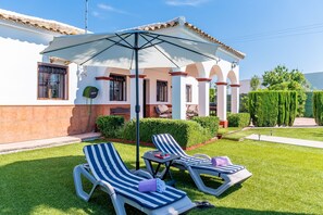 Eine Terrasse mit zwei Liegestühlen, einem Tisch und einem großen Sonnenschirm.