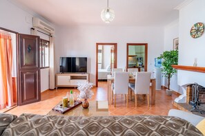 Ein Wohnzimmer mit Fernseher, Essbereich und einer Küche im Hintergrund.