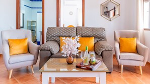 A living room with a sofa, two armchairs, a coffee table, a vase with flowers, and a wine bottle. - El Azahar Holiday Home (La Puebla de Cazalla)