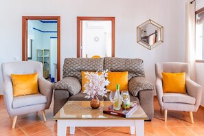 Ein Wohnzimmer mit einer Couch, zwei Sesseln, einem Couchtisch, einer Vase mit Blumen und einer Weinflasche.