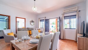 A dining area with a table set for four, a sofa, and a TV stand. - El Azahar Holiday Home (La Puebla de Cazalla)