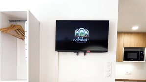 Ein modernes Zimmer mit einem an der Wand befestigten Fernseher, einem Holzschrank mit Schubladen und einer Küchenzeile inklusive Mikrowelle.