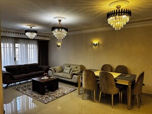 A living room with a sofa, a coffee table, a dining table with chairs, and two chandeliers. - Stylish 3-bedroom apartment with AC in Nasr city, Near to Cairo Airport (Nasr City)