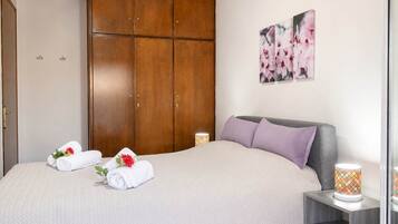 A hotel room with a bed, wooden wardrobe, and a wall-mounted picture of flowers.