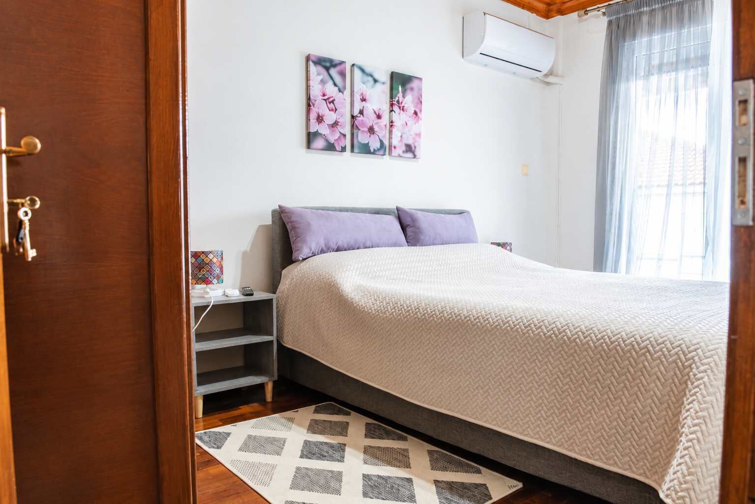 Een slaapkamer met een bed, nachtkastje, een wandairconditioner en een raam met gordijnen.