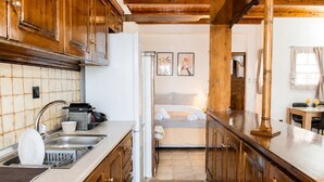 Una cocina con armarios de madera, un fregadero y un refrigerador. Hay una cama con cabecera blanca y una ventana con cortinas.