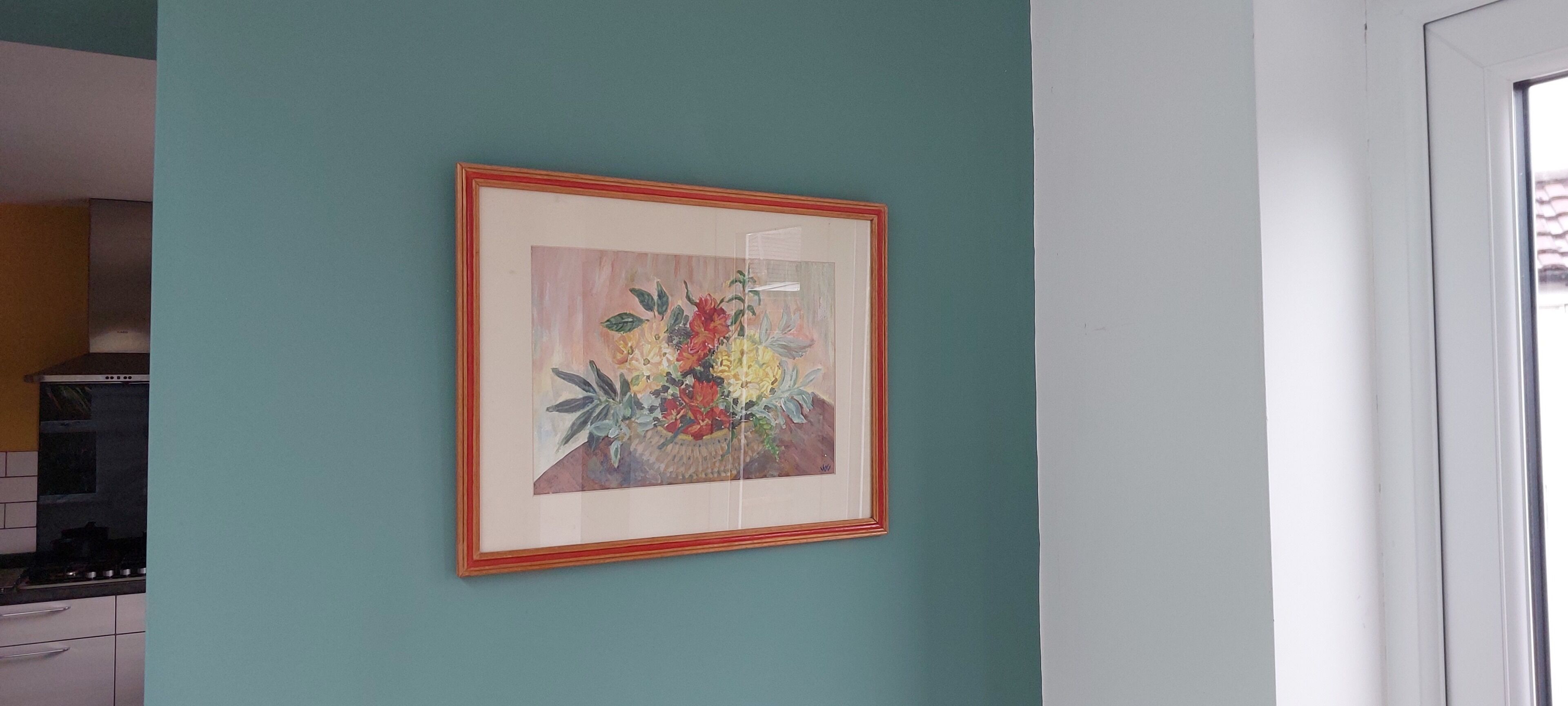 A framed floral artwork on a teal wall in a kitchen area.