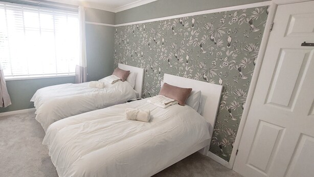 Ein Schlafzimmer mit zwei Einzelbetten, einem Fenster mit Vorhängen und floralem Wandpapier.