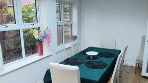 Ein Essbereich mit Tisch für vier Personen, umgeben von weißen Stühlen, unter einem Oberlicht mit Blick auf Grünflächen.