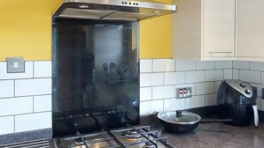 Eine Küche mit Gaskochfeld, Edelstahl-Dunstabzugshaube, weißen Schränken und einer gelben Akzentwand.