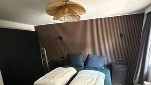 A modern bedroom with a bed, a bedside table, a lamp, and a radiator. - Intimate lodge (48 m²) for 2 people with full kitchen and spacious garden. Your four-legged friend is welcome too for an unforgettable Veluwe holiday. (Harderwijk)
