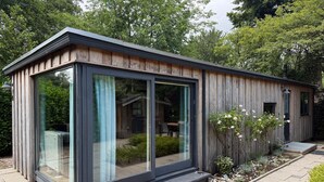 A modern wooden cabin with large glass windows, a small porch, and a garden area with plants and a bench. - Intimate lodge (48 m²) for 2 people with full kitchen and spacious garden. Your four-legged friend is welcome too for an unforgettable Veluwe holiday. (Harderwijk)