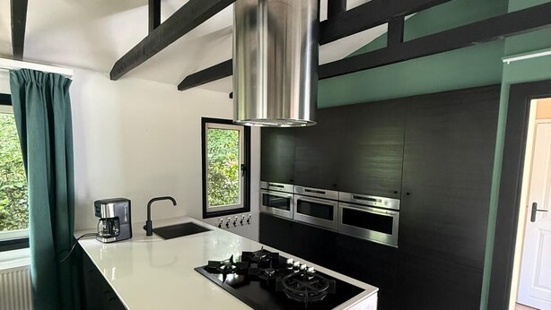 A modern kitchen with a central island, stainless steel appliances, and a black and white color scheme. - Intimate lodge (48 m²) for 2 people with full kitchen and spacious garden. Your four-legged friend is welcome too for an unforgettable Veluwe holiday. (Harderwijk)