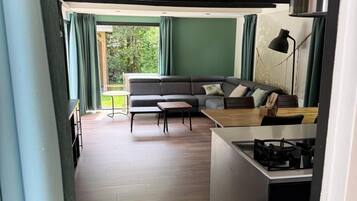 A compact living space with a kitchenette, a sofa, a dining table, and a view of greenery outside.