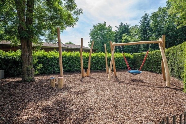 A wooden swing set in a backyard with mulch ground cover and a hedge in the background.