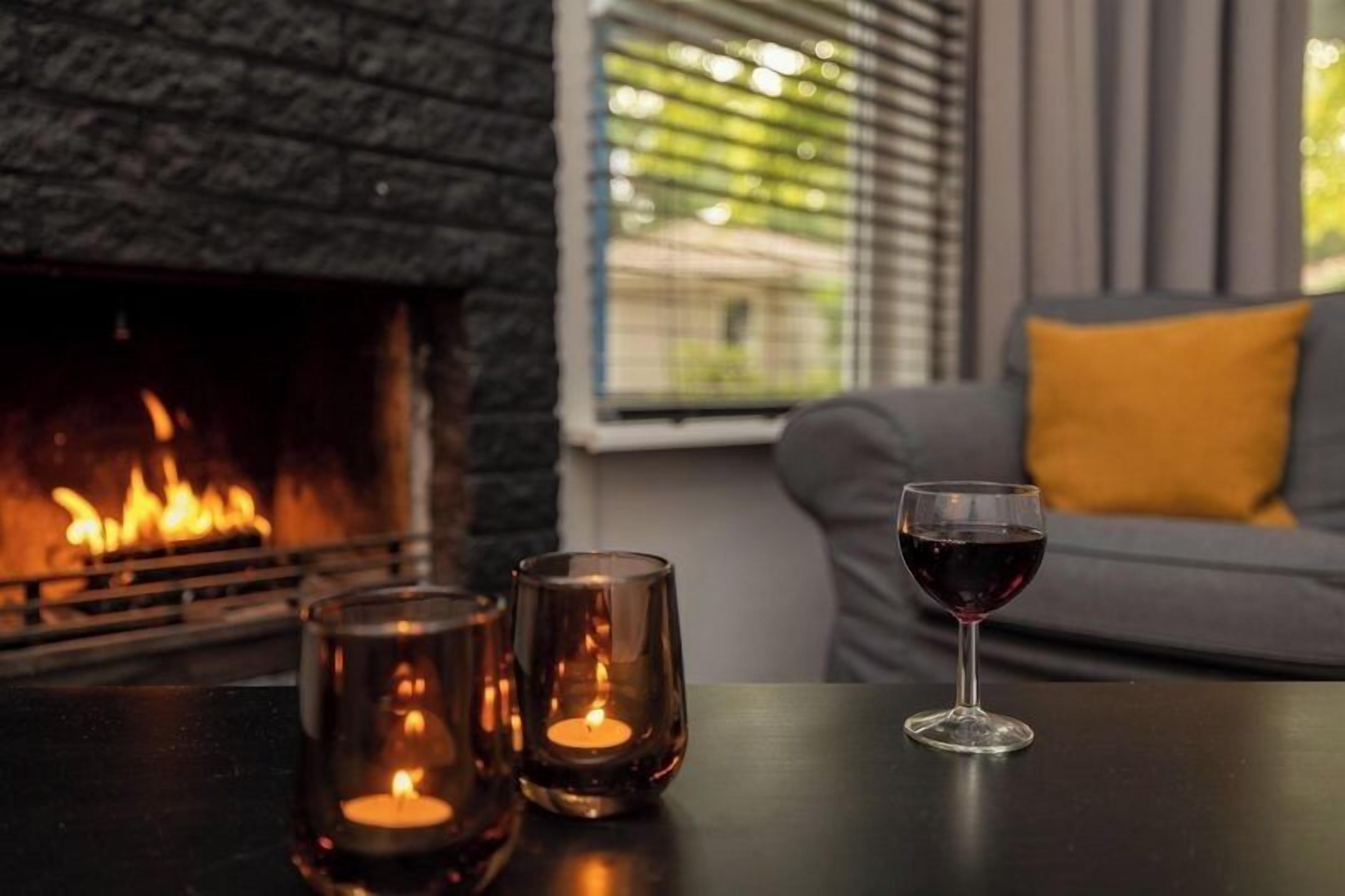 A fireplace, a sofa with a yellow cushion, and a table with glasses and a wine glass.