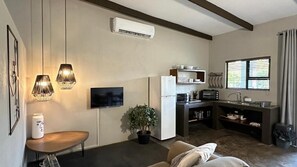 Cocina moderna con refrigerador, estufa y microondas. Hay una zona de comedor con mesa y sillas, una planta en maceta y un televisor montado en la pared.