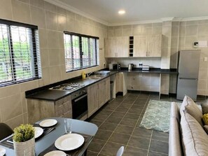 A modern kitchen with a dining area, featuring a sink, stove, and cabinets. - Spacious 2-Bedroom Apartment with Garden View in Hartbeespoort (Hartbeespoort)
