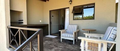 A covered outdoor area with a grill, two striped chairs, a small round table, and a sliding glass door.