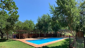 A backyard with a swimming pool, surrounded by trees and a brick wall. - Spacious 2-Bedroom Apartment with Garden View in Hartbeespoort (Hartbeespoort)