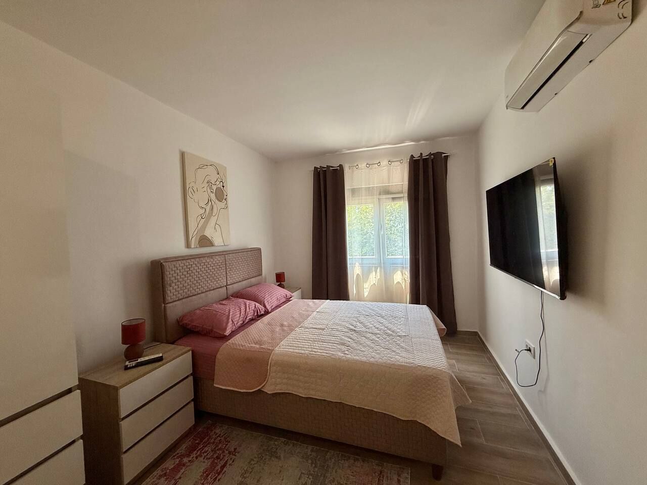 Une chambre à coucher avec un lit, une table de chevet, un téléviseur et une fenêtre avec des rideaux.