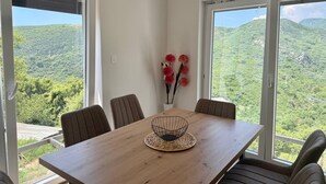 A dining area with a wooden table, four chairs, a woven placemat, and a vase with red flowers. - Top Hill Villa AnastaZija, Ivanovici, Budva (Boreti)
