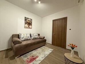 Ein Wohnzimmer mit einem braunen Sofa, gemusterten Kissen, einem Teppich, einer Holztür und einem kleinen Tisch mit einem Blumenstrauß.