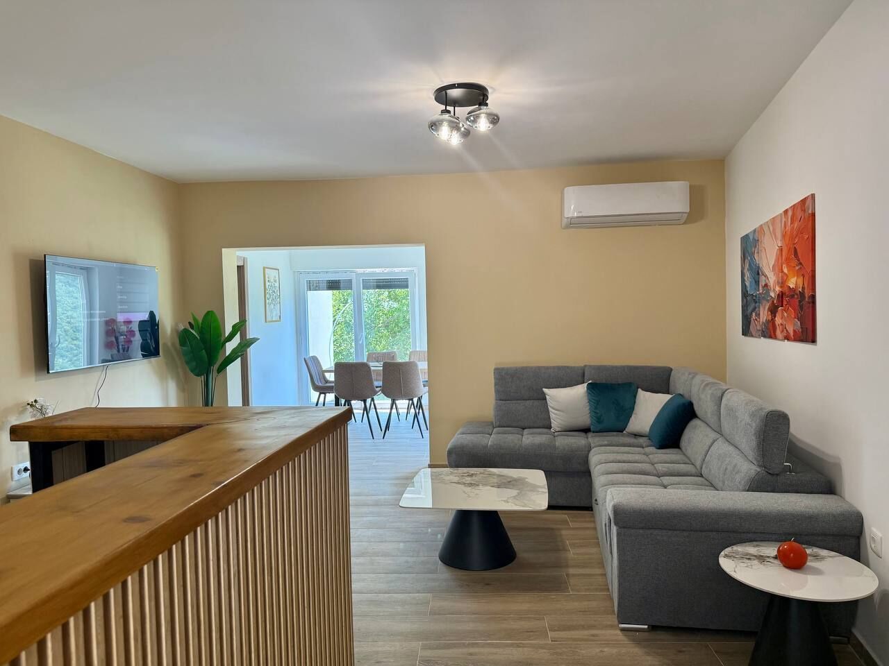 Un salon moderne avec un canapé gris, un comptoir d’accueil en bois, une table basse en marbre et un coin repas avec des chaises.