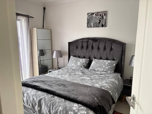 Ein Schlafzimmer mit einer gepolsterten Kopfteile, einem Bett mit blumigem Muster, einem Nachttisch mit einer Lampe, einem Spiegel und einem Zebrabild an der Wand.