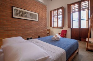 Une chambre d’hôtel avec un mur en briques, un lit avec une literie blanche et bleue, une chaise rouge et des portes en bois.