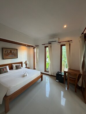 A hotel room with a large bed, a desk, and a chair. There is a window with curtains and an air conditioning unit on the wall. - A quiet room with balcony in Nyuh Kuning Ubud (Ubud)