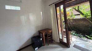 Ein Zimmer mit einer Schiebeglastür, die zu einem Garten führt, einem kleinen Tisch mit Stühlen, einem schwarzen Koffer und einer Wand-Klimaanlage.