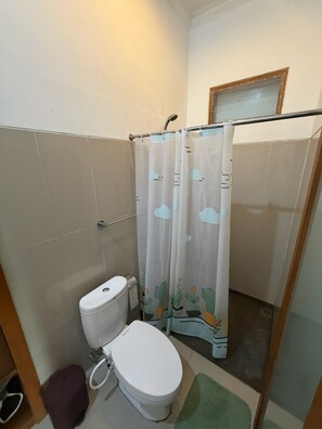 Ein Badezimmer mit Toilette, einer Duschvorhang mit Kaktusmuster und einem kleinen Teppich.