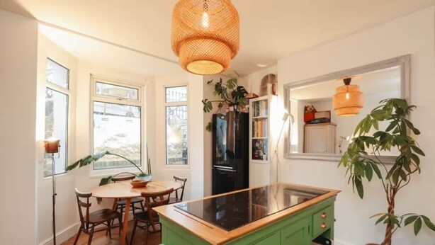 Een keuken met een groen kookeiland, houten stoelen en een groot raam.