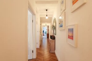 Ein Korridor mit Fischgrätparkett, einem Blumentopf und gerahmten Kunstwerken an den Wänden.