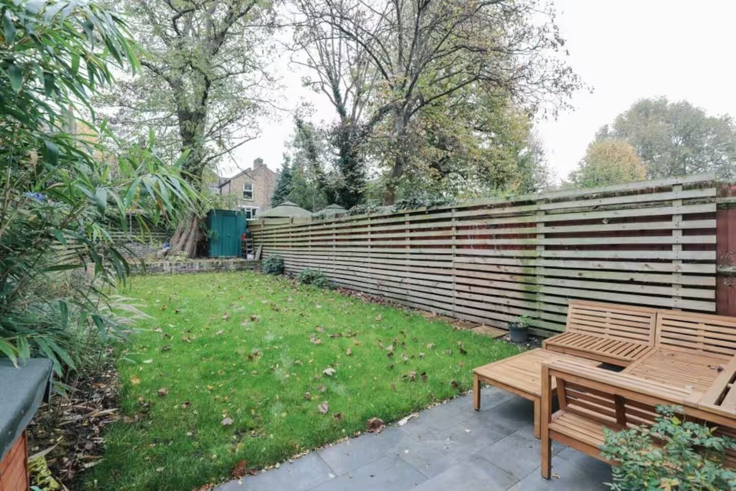 Een achtertuin met een houten omheining, een gazon en een houten tuimbank, plus een tuinhuis.
