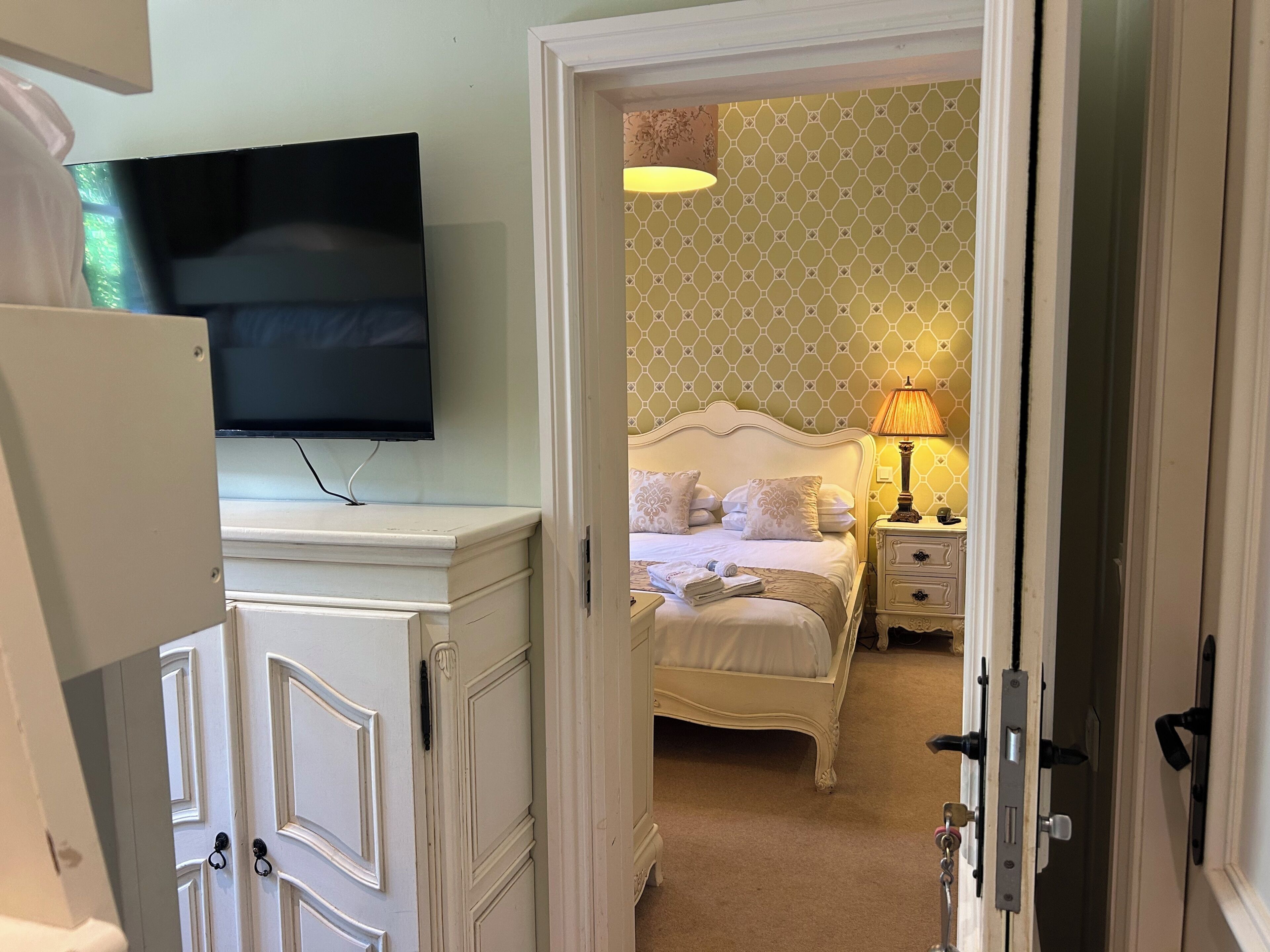 A hotel room with a bed, a bedside lamp, a television on a dresser, and a patterned wall.