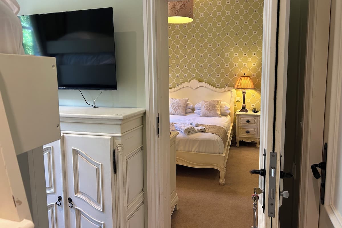 Una habitación de hotel con cama, lámpara de noche, televisión sobre un aparador y pared con diseño.