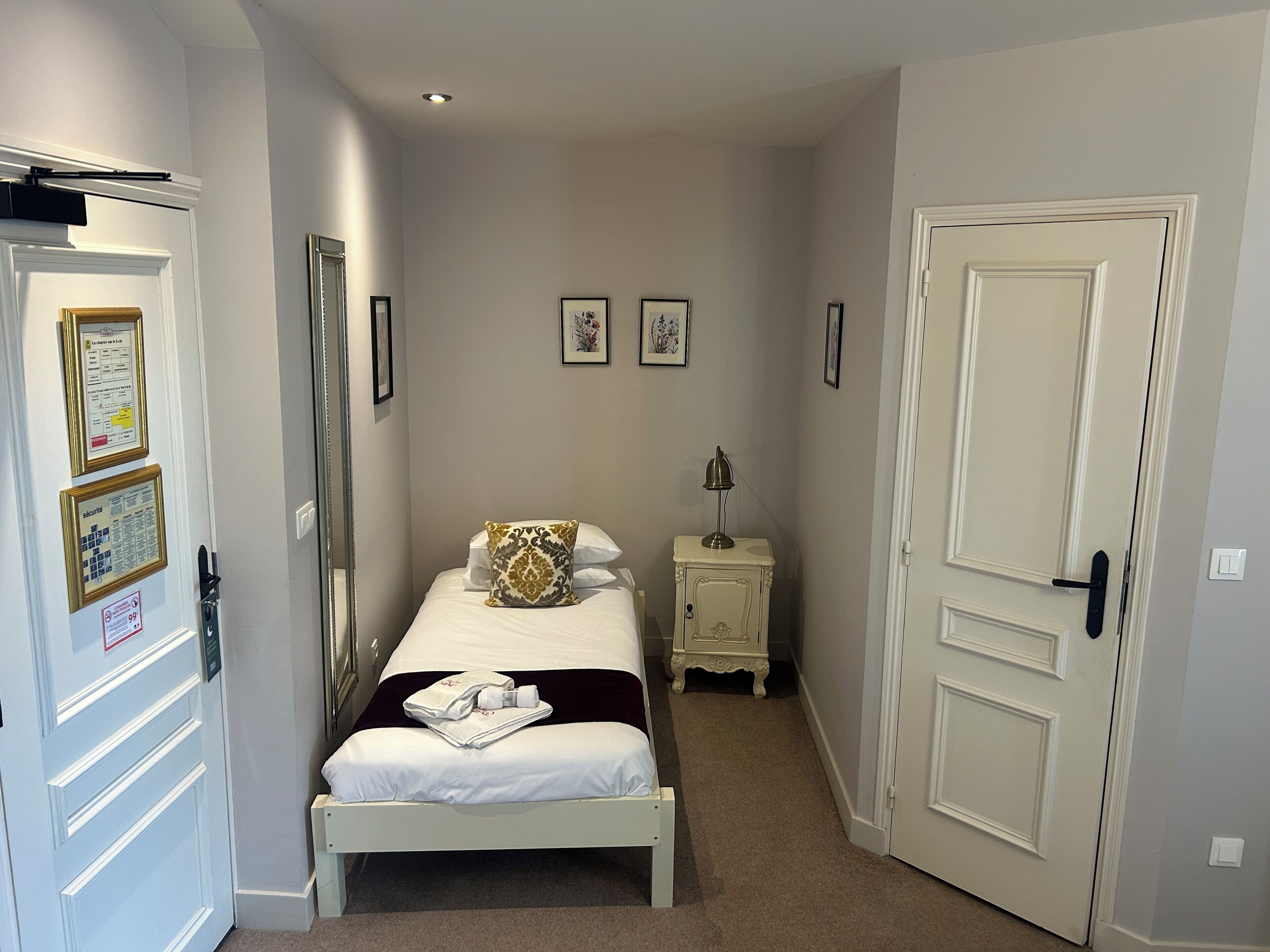 Una camera d'albergo modesta con un letto, un comodino, una lampada e una porta.
