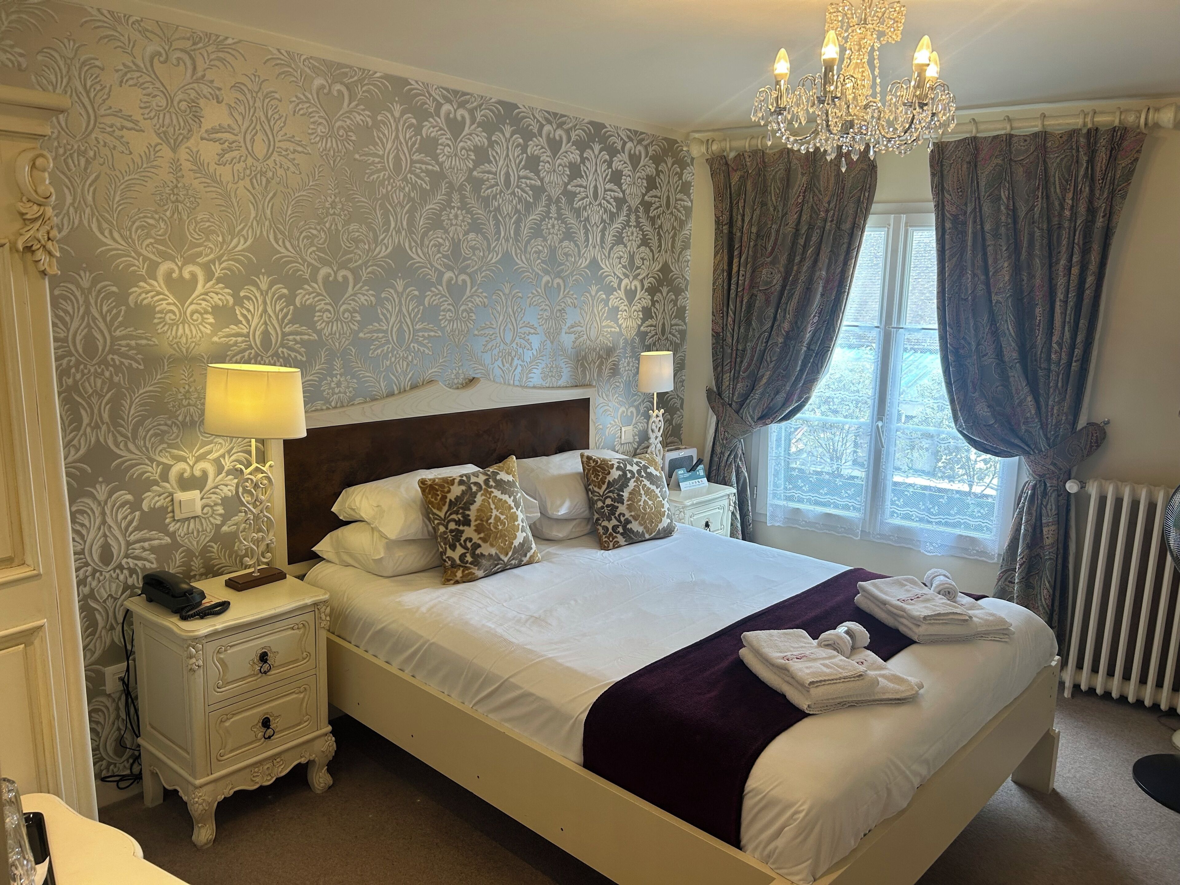 A neatly arranged bedroom with a large bed, two bedside tables, a chandelier, and a window with curtains.