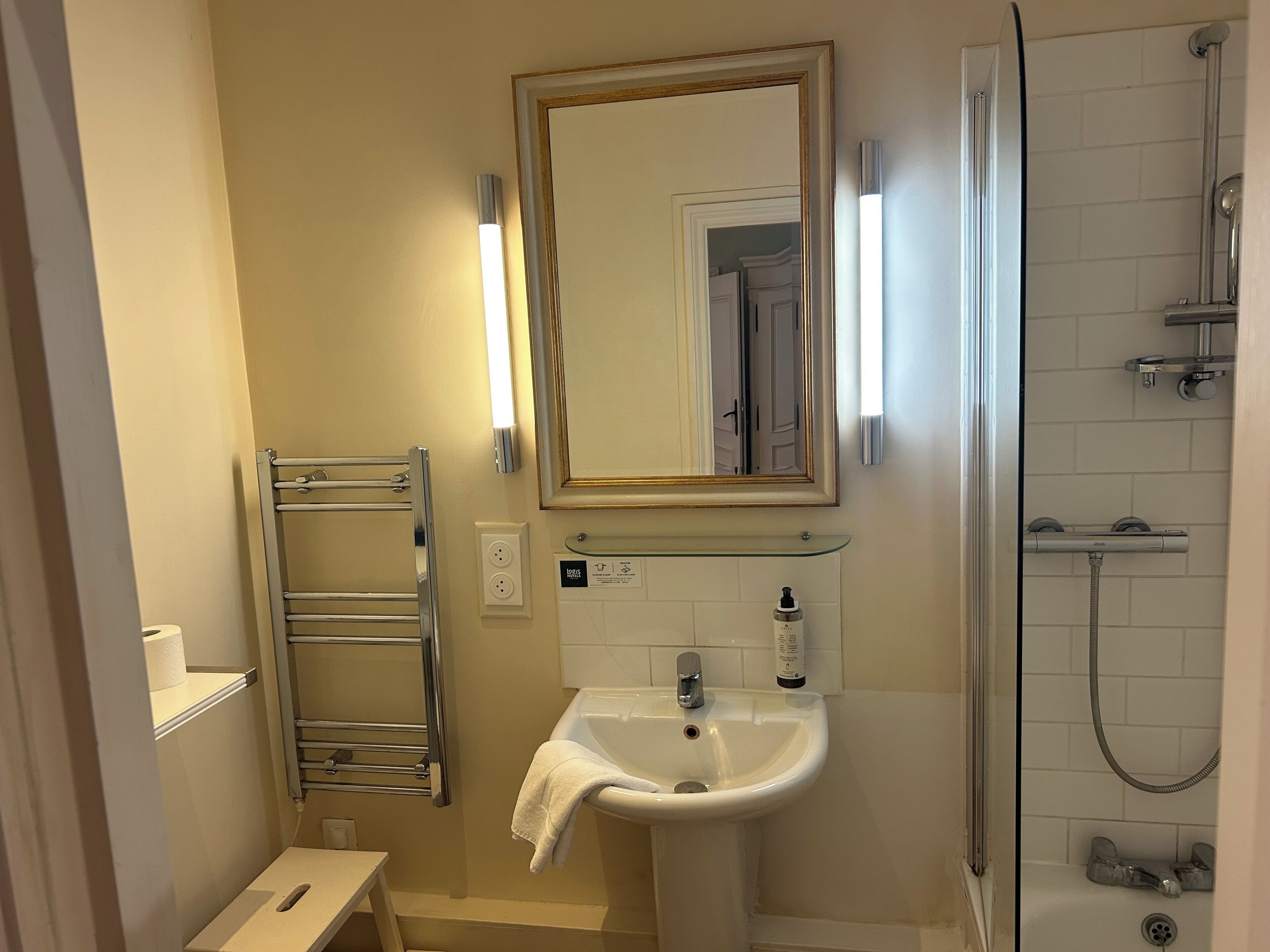 Une salle de bain avec un lavabo blanc, un miroir, un porte-serviettes et un espace douche.