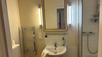 Une salle de bain avec un lavabo blanc, un miroir, un porte-serviettes et un espace douche.