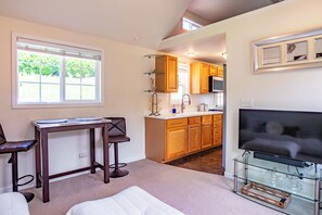 A living room with a TV, a dining table, and a kitchen in the background. - Upscale Riverfront Getaway Cottage (Arlington)