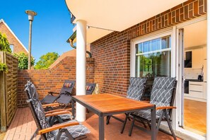 Eine Terrasse im Freien mit Tisch und Stühlen, eine Ziegelwand und eine Schiebetür zu einer Küche.